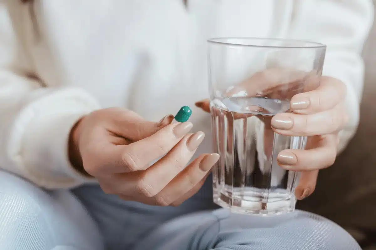 Close-up of hands holding a green capsule and a glass of water.
