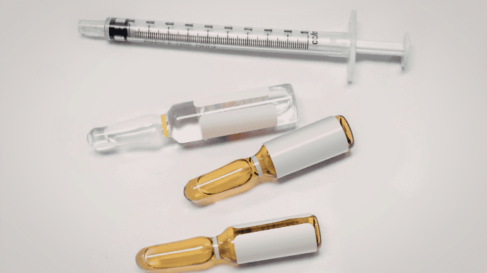 A sterile layout featuring a single-use syringe and four glass ampoules containing clear and amber-colored liquids.