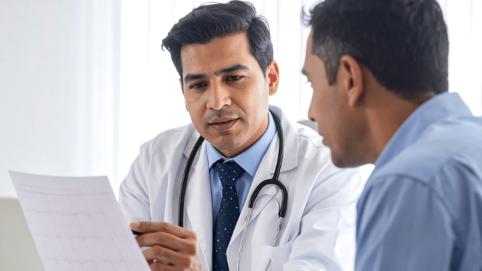 A male doctor in a white coat consulting with a patient.