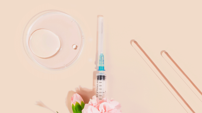 A top-down, minimalist aesthetic composition on a beige background featuring medical and laboratory elements. It includes a glass petri dish with a clear liquid droplet, a sterile syringe with a needle cap, and two glass stirring rods.