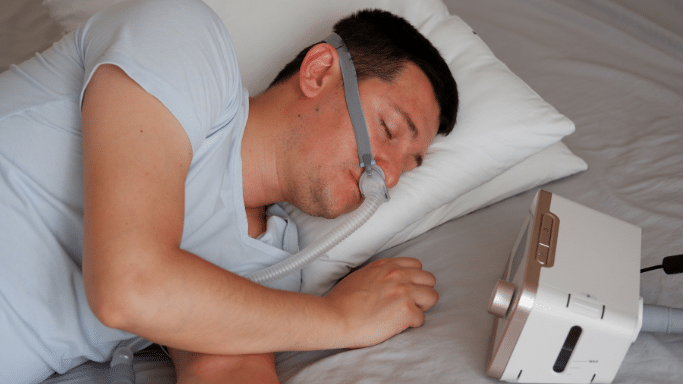 A man sleeping while wearing a CPAP nasal mask connected to a bedside machine.