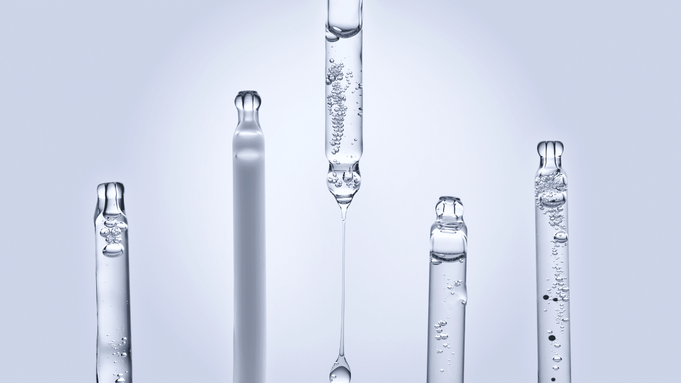 Five glass pipettes containing clear liquids with air bubbles against a light blue background.