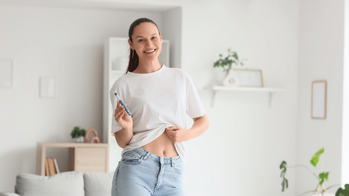 Woman in a white tee holding a medical injection pen near her waist.