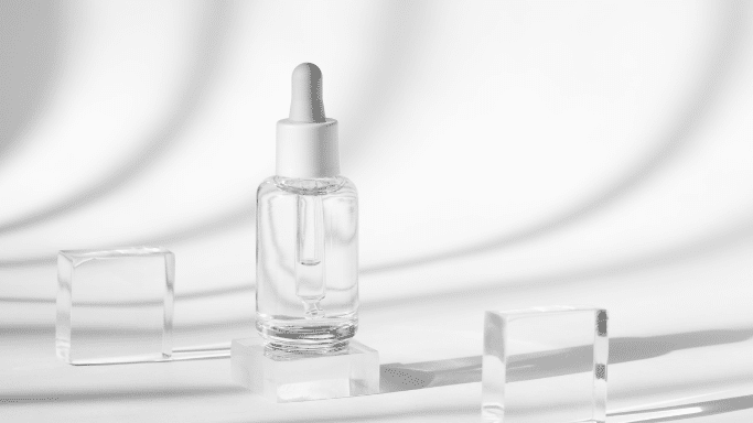 Clear serum bottle with a dropper on a glass block with soft shadows.