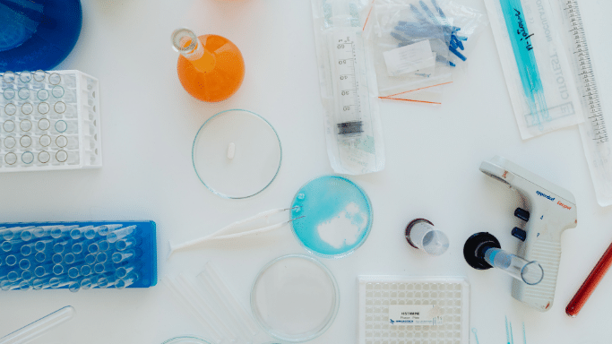 Top-down view of a lab table with petri dishes, test tubes, and pipettes.