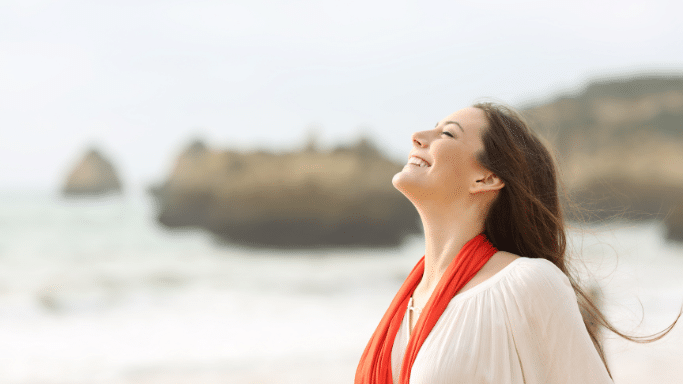 Profile of a woman in an orange scarf smiling toward the sky at the beach.