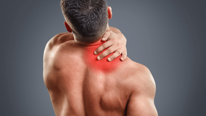 A rear view of a shirtless, muscular man clutching the back of his neck with his right hand. A bright red, glowing circular overlay is centered on his lower neck and upper trapezius area, indicating a focal point of pain or inflammation.