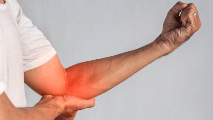 A person’s arm bent at the elbow, with their hand clenched in a fist. A bright red, glowing overlay covers the outer elbow area, highlighting a specific point of joint or tendon pain.