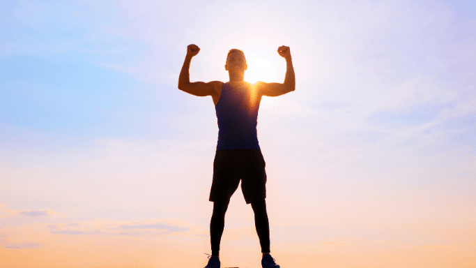 A silhouette of a muscular person standing triumphantly with both arms flexed in a "double biceps" pose against a bright, hazy sunrise or sunset.