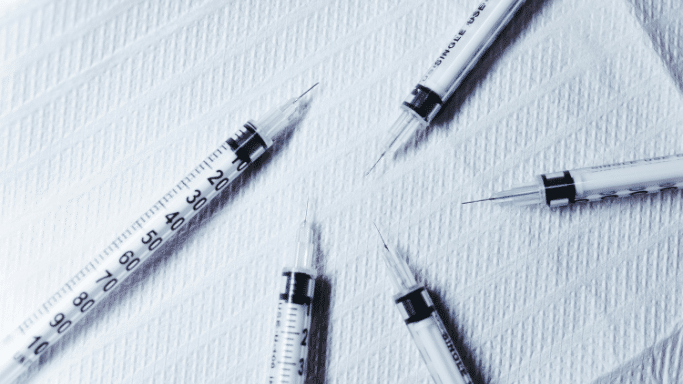 top-down view of five medical syringes with needles attached, arranged in a circular pattern on a textured white surface.