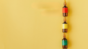 Three glass ampoules stacked vertically against a solid yellow background. Each ampoule has a different colored band: red on the top one, yellow on the middle, and green on the bottom.