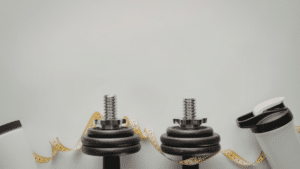 A minimalist fitness-themed flat lay against a light grey background. In the lower half, there are two black adjustable dumbbells, a yellow measuring tape curled around them, and two white protein shakers on either side. The top half of the image is empty space.