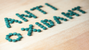 Small, round, dark green supplement tablets arranged on a light wood surface to spell out the word "ANTIOXIDANT" in two lines.