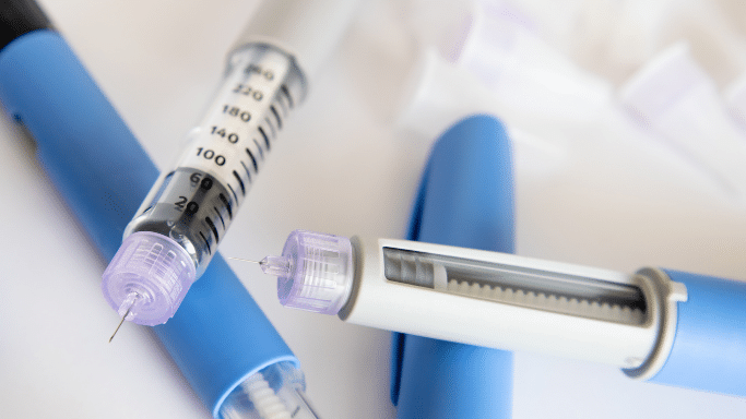 One pen is in the foreground with its cap off, revealing a very short, fine needle. In the background, extra needle caps are scattered on a white surface.