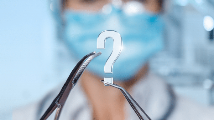 A conceptual image showing a person in a medical mask and goggles in a blurred background. In the foreground, surgical forceps hold a small, translucent 3D question mark symbol.