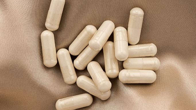 A cluster of white or light beige capsule pills scattered across a shimmering, beige satin fabric.