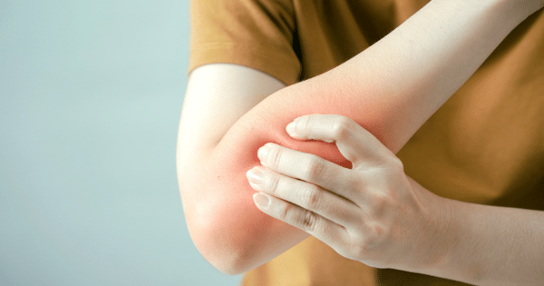 A close-up of a person in a brown shirt holding their inner elbow joint with their hand, with a red glow overlaid on the area to signify joint or muscle pain.