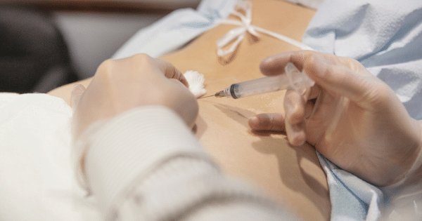 Close-up shot of a healthcare provider's hands in clear gloves administering an injection with a syringe into a patient's bare back.