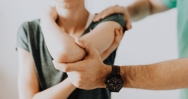 Close-up of a physical therapist's hands gently supporting and guiding a patient's bent arm and elbow during a rehabilitation session.