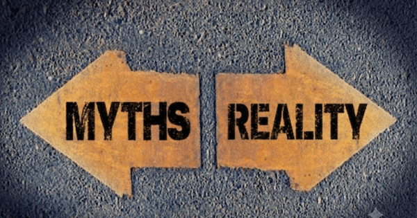 Two weathered arrow shapes painted on asphalt pointing in opposite directions; the left arrow reads "MYTHS" and the right arrow reads "REALITY".