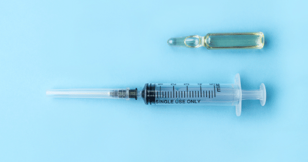A clear medical syringe labeled "SINGLE USE ONLY" and a small glass ampoule containing a yellowish liquid, arranged flat against a solid light-blue background.