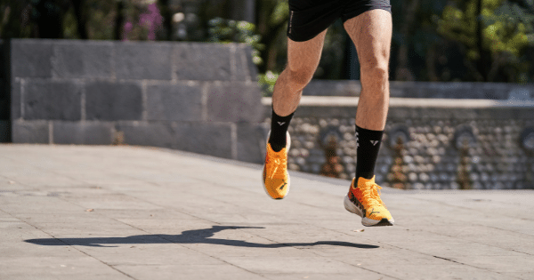 Lower-body view of a runner's legs mid-stride wearing bright orange running shoes.