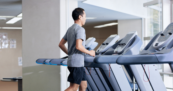 Side view of a man in workout clothes jogging on a treadmill inside a modern indoor gym facility.