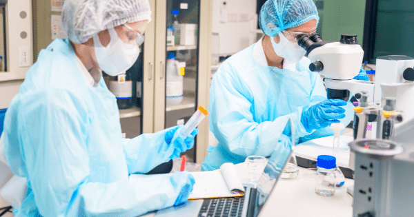 Two scientists wearing protective suits and masks conducting research with a microscope and test tubes in a lab.