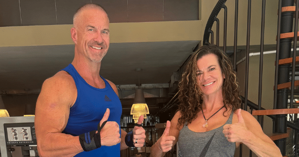A athletic man and woman giving thumbs-up gestures inside a workout facility.
