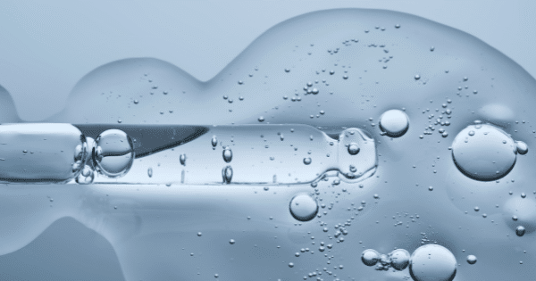 Macro photo of a glass skincare dropper releasing a clear gel liquid with air bubbles.