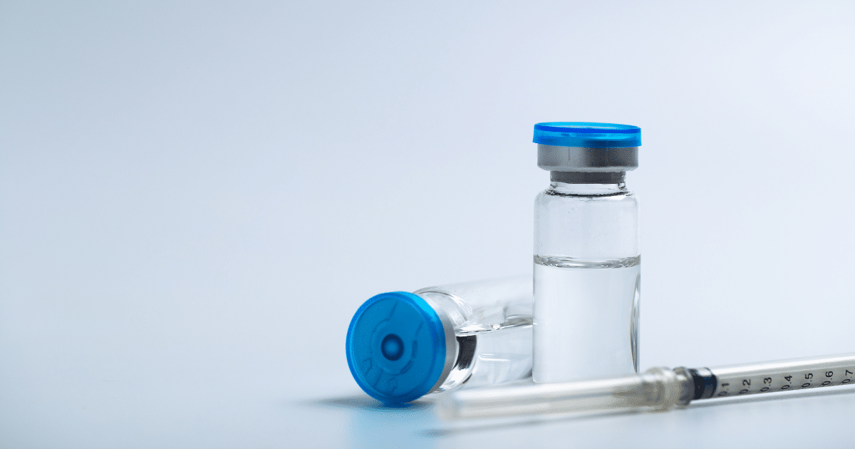 Two glass liquid vials with blue caps next to a medical syringe.