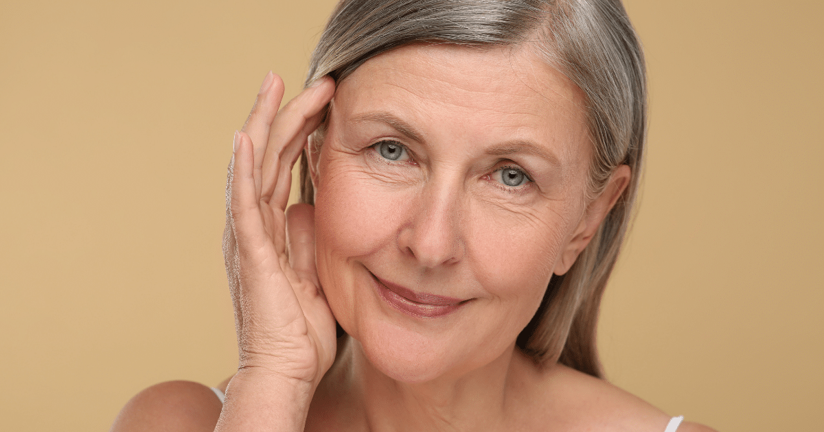 Close-up portrait of a smiling mature woman gently touching her temple.