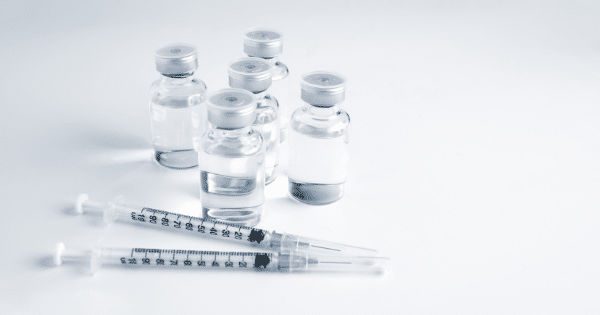Small glass medicine vials standing beside two syringes.