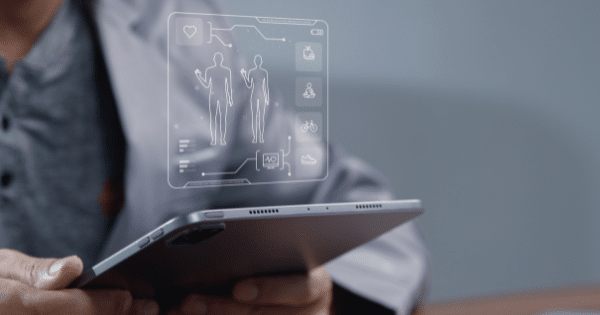 Side-view close-up of a healthcare provider holding a digital tablet, which projects a clean, minimalist hologram outlining male and female body figures alongside health and lifestyle icons.