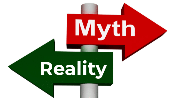 A signpost with two opposing directional arrows mounted on a pole: a red arrow pointing right labeled "Myth" and a green arrow pointing left labeled "Reality."