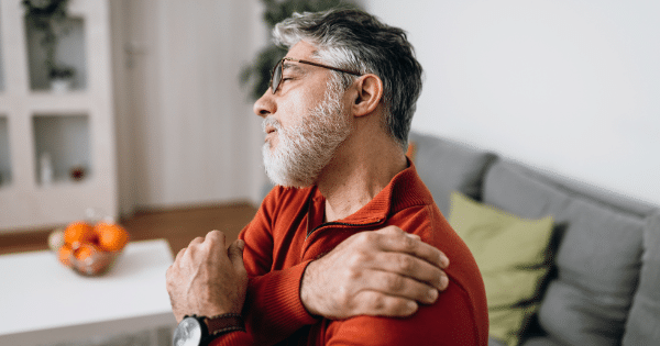 Older man wincing while holding his aching shoulder at home.
