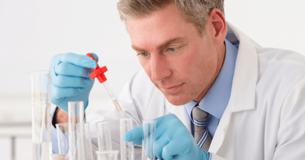 Scientist using a liquid dropper over laboratory test tubes.