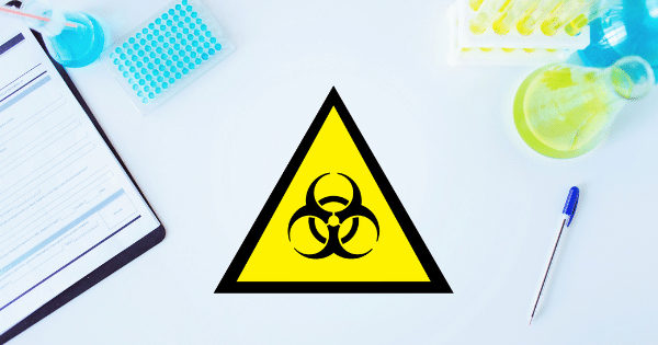 A flat-lay medical laboratory setup featuring a clipboard, beakers, test tubes, and a prominent biohazard warning symbol in the center.