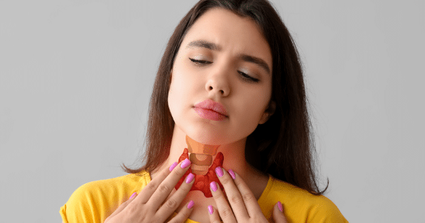 A woman in a yellow shirt holding her neck with both hands, with an anatomical illustration of a thyroid gland superimposed over her throat.