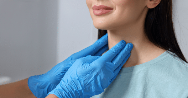 A clinician wearing blue medical gloves examining a patient’s neck area by gently palpating the throat.