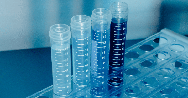 Four graduated plastic test tubes filled with varying shades of clear to dark blue liquid sitting in a lab rack.