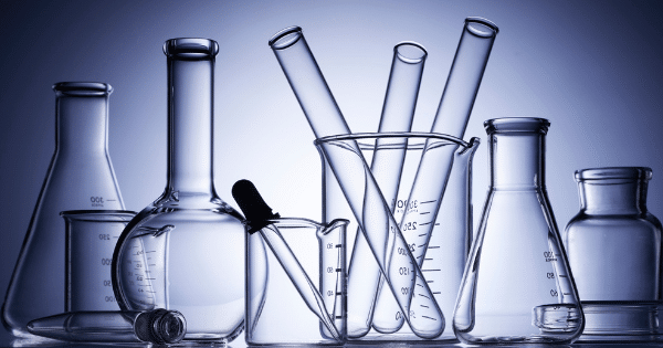 An assortment of clean, empty glass laboratory equipment including beakers, flasks, test tubes, and a glass pipette against a soft blue background.