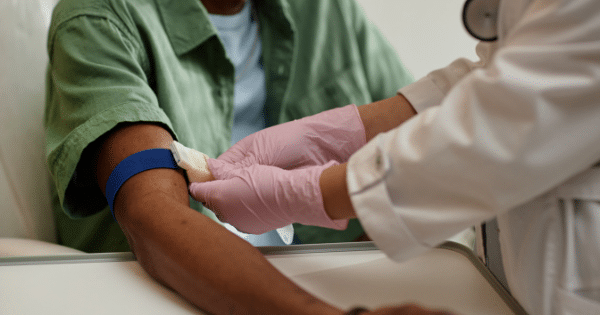 Close-up of a healthcare professional in pink gloves applying a blue tourniquet to a patient's arm to prepare for a blood draw.