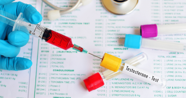A gloved hand draws blood from a vial labeled "Testosterone - Test" using a syringe against a backdrop of medical lab forms.