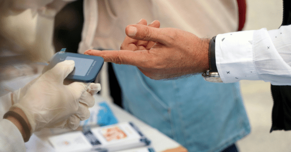 A gloved healthcare worker inserting a test strip with a blood sample into a portable glucometer to measure a patient's blood sugar level.