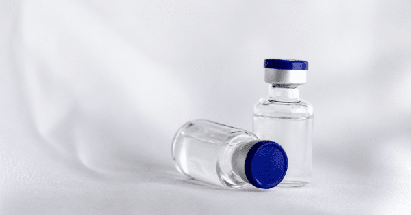 Two clear medication vials with blue caps resting on a white fabric surface.