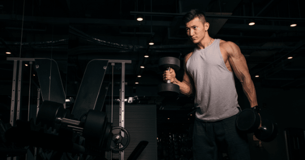 Man lifting dumbbells during a workout in a dimly lit gym space.