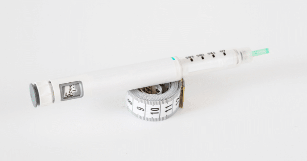 An insulin or GLP-1 injection pen resting on top of a rolled-up white measuring tape over a clean white surface.