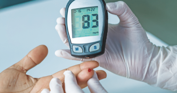 A healthcare worker in white gloves testing a patient's blood glucose level using a digital meter.