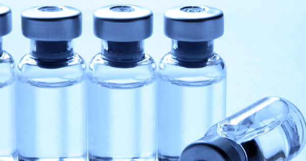 A line of clear glass liquid vials with silver caps, with one vial lying down on its side.